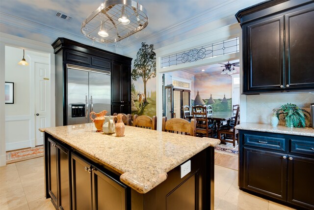 kitchen with light tile floors, light stone counters, ornamental molding, built in fridge, and a center island