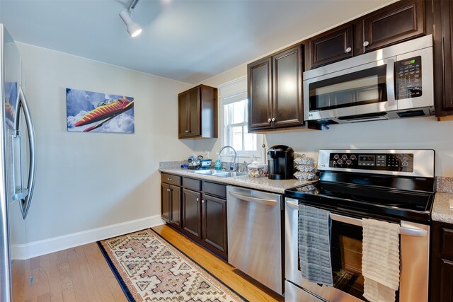 kitchen featuring appliances with stainless steel finishes, track lighting, sink, light wood-type flooring, and dark brown cabinets