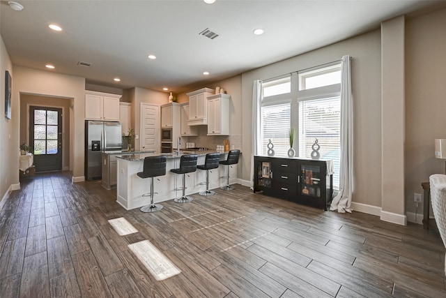 kitchen with a kitchen bar, dark wood-type flooring, appliances with stainless steel finishes, white cabinets, and dark stone countertops