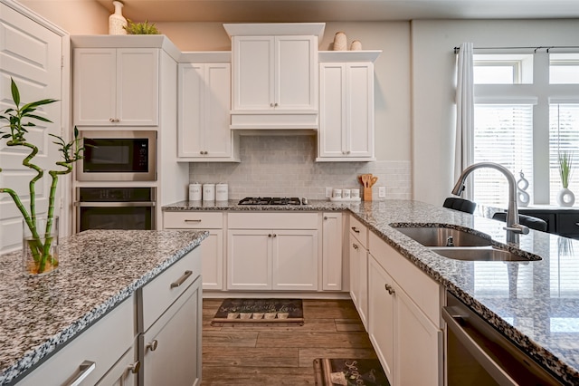 kitchen with white cabinetry, stainless steel appliances, light stone countertops, backsplash, and sink