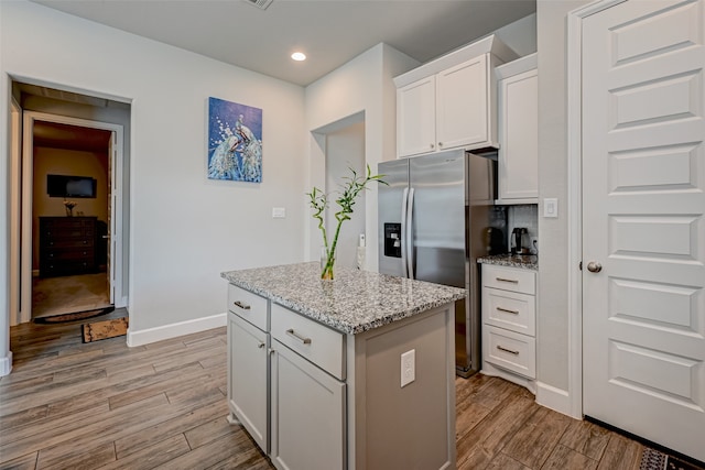 kitchen featuring white cabinets, a kitchen island, light hardwood / wood-style flooring, light stone countertops, and stainless steel fridge with ice dispenser