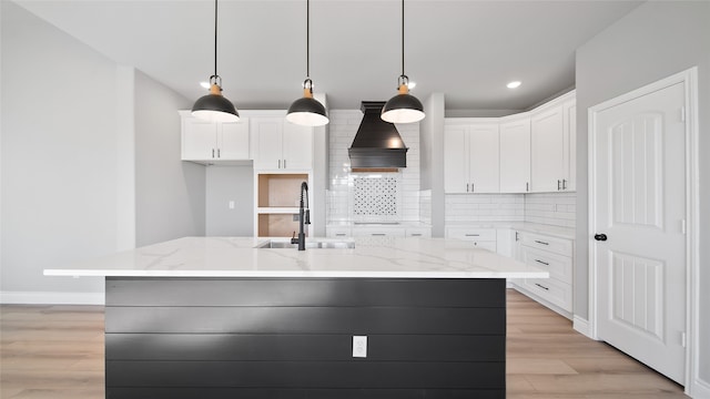 kitchen featuring decorative light fixtures, custom range hood, tasteful backsplash, and a kitchen island with sink