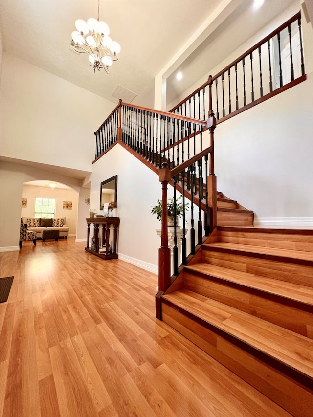 staircase featuring a towering ceiling, a notable chandelier, and light hardwood / wood-style flooring