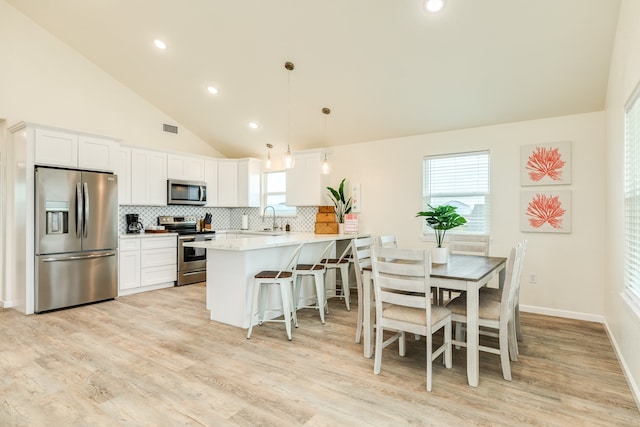 kitchen with hanging light fixtures, stainless steel appliances, backsplash, and white cabinetry