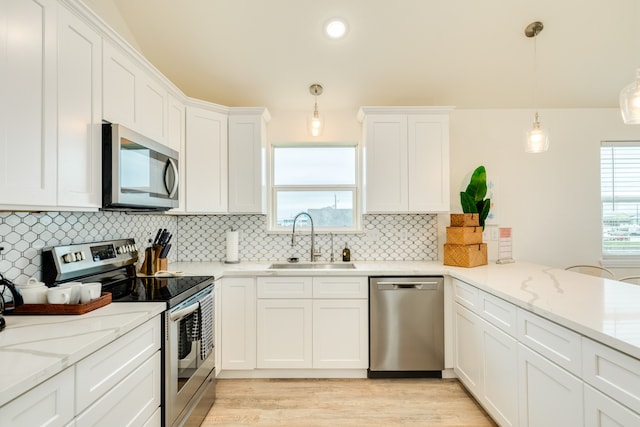 kitchen featuring decorative light fixtures, appliances with stainless steel finishes, white cabinets, light hardwood / wood-style flooring, and sink