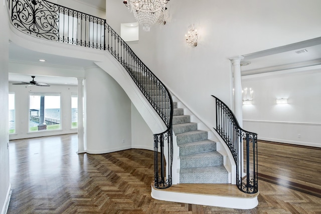 staircase with ornate columns, ceiling fan, parquet floors, a towering ceiling, and ornamental molding