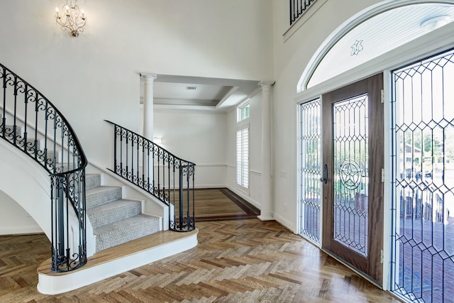 entrance foyer with a notable chandelier, parquet flooring, a towering ceiling, and decorative columns