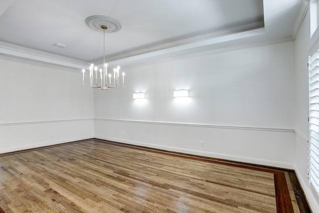 spare room with a raised ceiling, wood-type flooring, crown molding, and an inviting chandelier