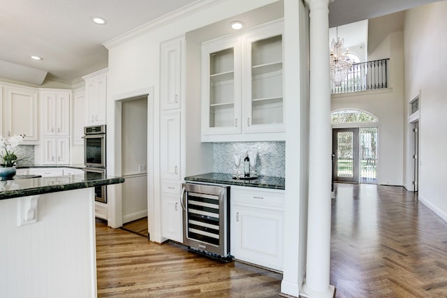 kitchen featuring decorative columns, wine cooler, dark stone countertops, and white cabinets