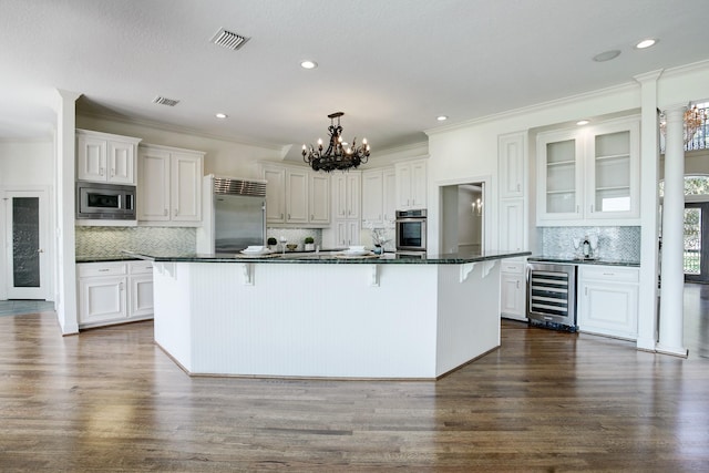 kitchen featuring a breakfast bar area, built in appliances, white cabinetry, and beverage cooler