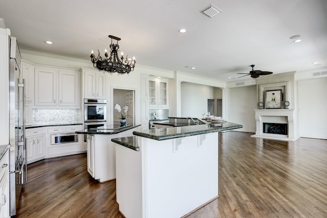 kitchen featuring a kitchen breakfast bar, ceiling fan with notable chandelier, decorative light fixtures, a center island, and white cabinetry