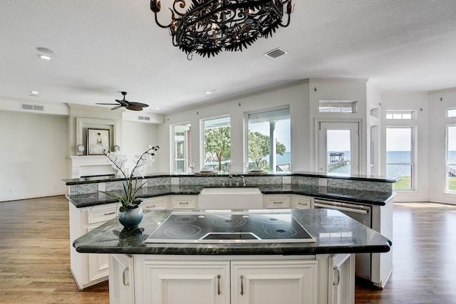 kitchen with black electric stovetop, sink, hardwood / wood-style flooring, an island with sink, and white cabinetry