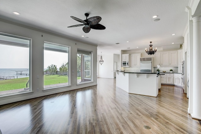 kitchen featuring white cabinetry, backsplash, built in appliances, an island with sink, and a water view