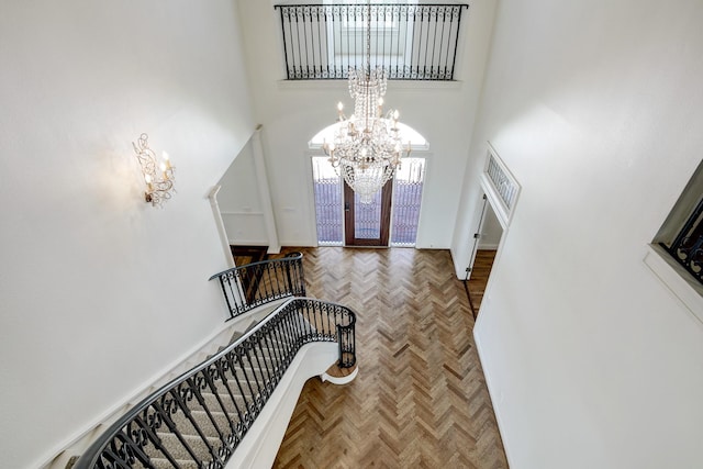 foyer entrance featuring parquet flooring, french doors, a towering ceiling, and an inviting chandelier