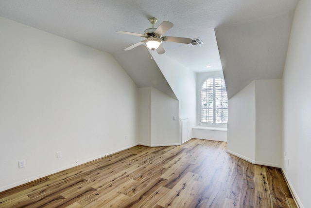 additional living space with a textured ceiling, ceiling fan, light hardwood / wood-style flooring, and vaulted ceiling