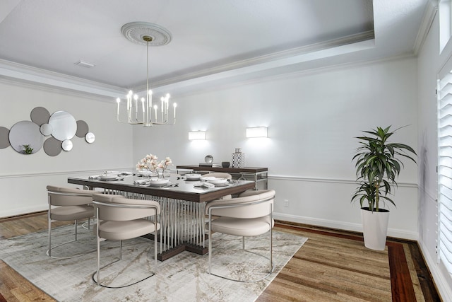 dining space with hardwood / wood-style floors, a tray ceiling, ornamental molding, and a notable chandelier