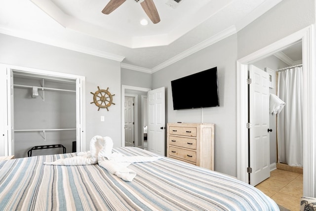 tiled bedroom with a closet, a tray ceiling, ceiling fan, and ornamental molding