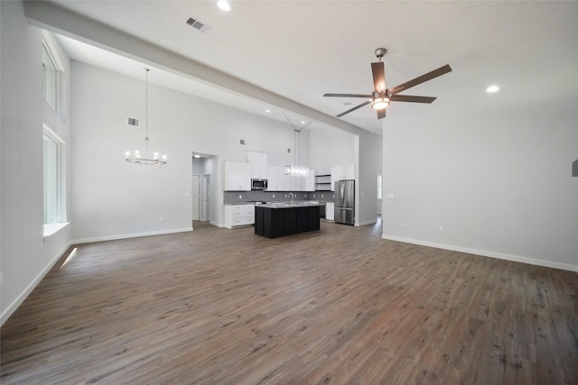 unfurnished living room with ceiling fan with notable chandelier, visible vents, dark wood-style flooring, and baseboards