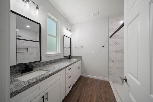 bathroom with visible vents, a sink, a marble finish shower, double vanity, and baseboards