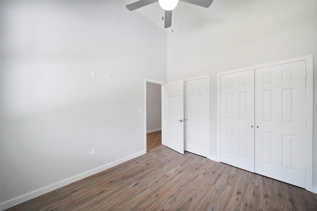 unfurnished bedroom with multiple closets, a ceiling fan, wood finished floors, baseboards, and a towering ceiling