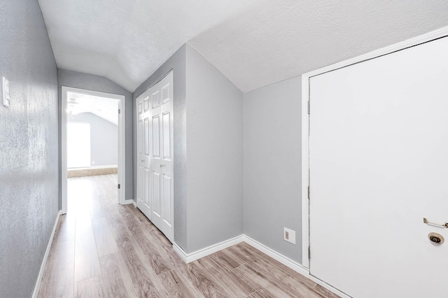 hallway with a textured ceiling, lofted ceiling, and light wood-type flooring