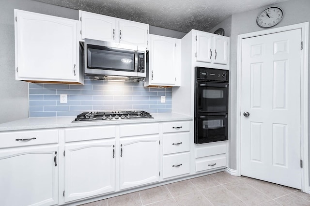 kitchen featuring light tile patterned floors, white cabinetry, stainless steel appliances, decorative backsplash, and a textured ceiling