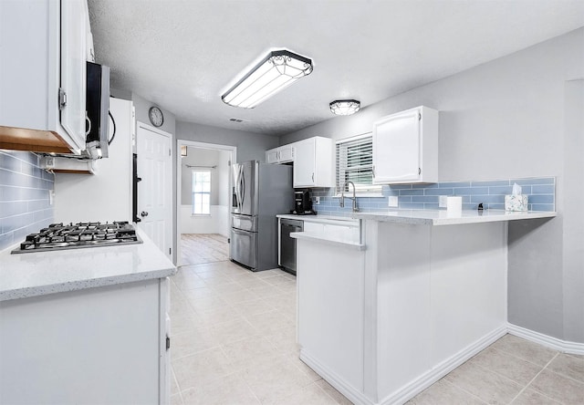 kitchen featuring white cabinetry, decorative backsplash, stainless steel appliances, and light stone countertops