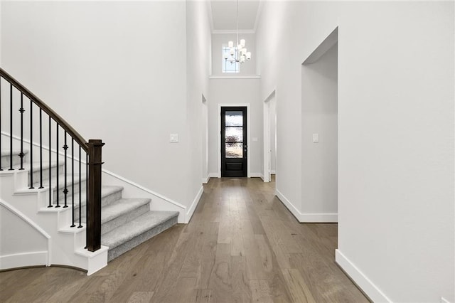 foyer featuring an inviting chandelier, hardwood / wood-style flooring, crown molding, and a high ceiling