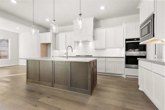 kitchen featuring white cabinetry, decorative light fixtures, stainless steel appliances, and an island with sink