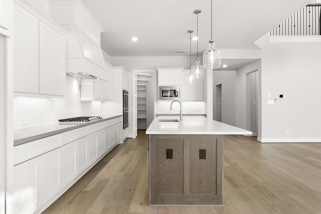 kitchen featuring appliances with stainless steel finishes, decorative light fixtures, white cabinetry, an island with sink, and sink