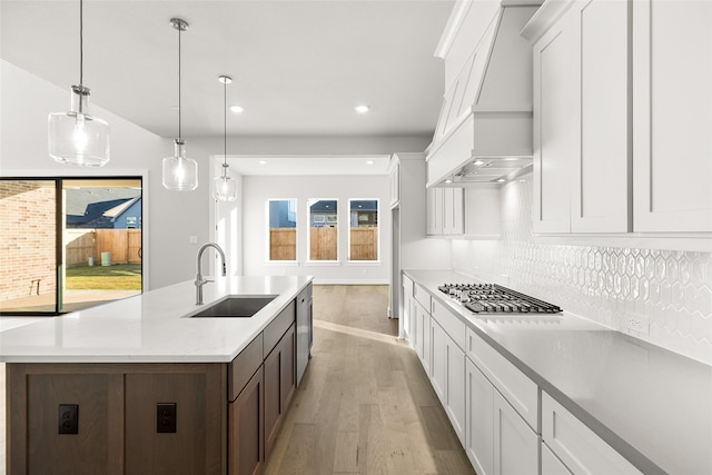 kitchen with sink, white cabinetry, a center island with sink, decorative light fixtures, and custom exhaust hood