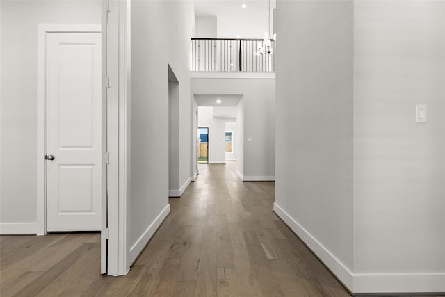 corridor featuring a towering ceiling, light wood finished floors, and baseboards