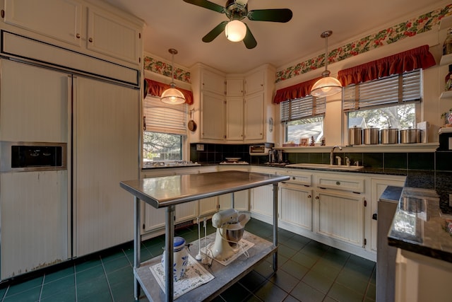 kitchen with paneled built in fridge, ceiling fan, sink, dark tile flooring, and tasteful backsplash