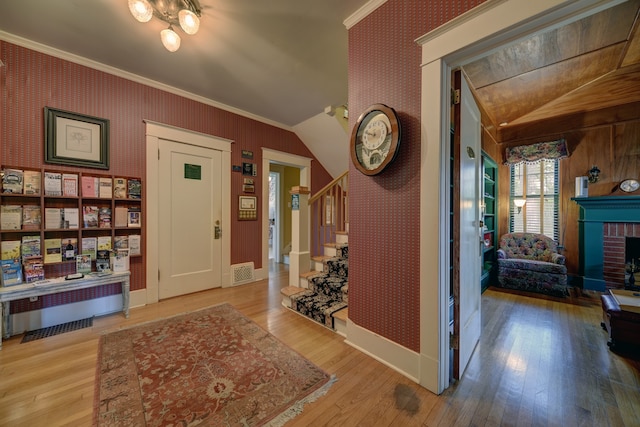 entrance foyer featuring a brick fireplace, ornamental molding, light hardwood / wood-style floors, and lofted ceiling