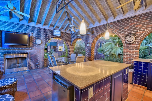 kitchen with ceiling fan, a kitchen island, beamed ceiling, exterior fireplace, and tile floors