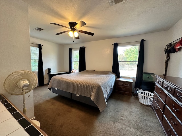 bedroom featuring ceiling fan, dark colored carpet, and a textured ceiling