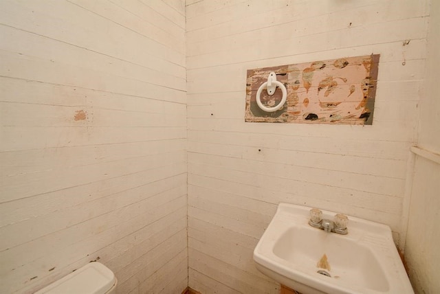 bathroom with wood walls, sink, and toilet