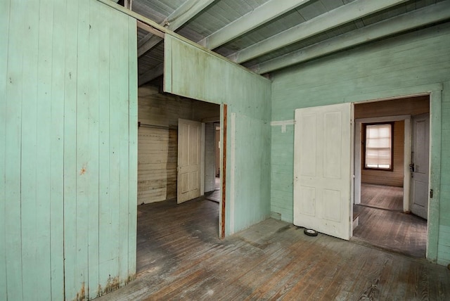 unfurnished room with wood walls, beam ceiling, and hardwood / wood-style flooring