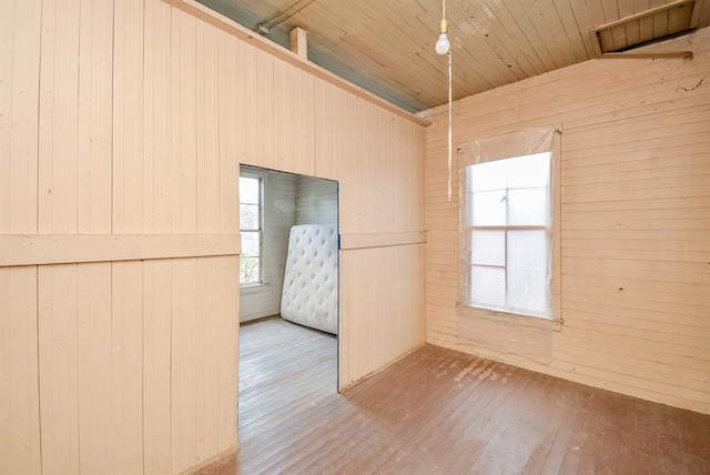 unfurnished room with light wood-type flooring, wooden walls, and wooden ceiling