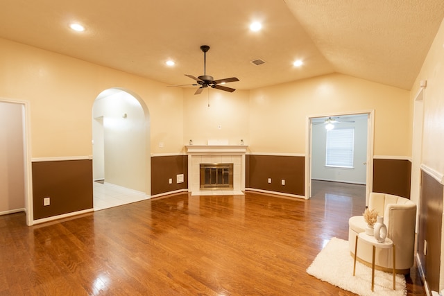 unfurnished living room with a tile fireplace, a textured ceiling, wood-type flooring, lofted ceiling, and ceiling fan