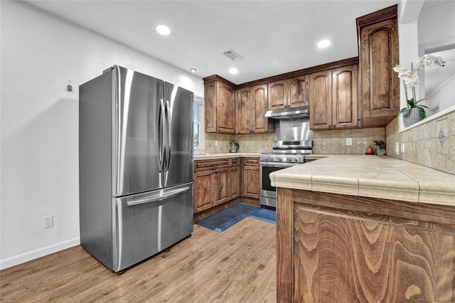 kitchen with tile counters, appliances with stainless steel finishes, backsplash, and light wood-type flooring