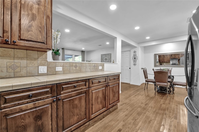 kitchen featuring light hardwood / wood-style flooring, tile countertops, tasteful backsplash, and refrigerator