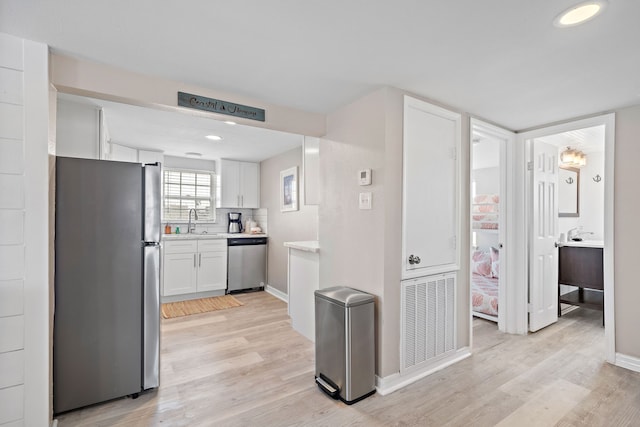 kitchen featuring appliances with stainless steel finishes, light wood-type flooring, backsplash, sink, and white cabinetry