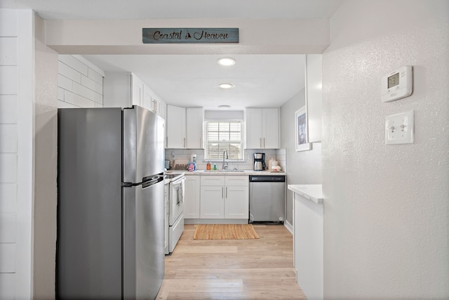 kitchen with white cabinetry, backsplash, light hardwood / wood-style floors, sink, and stainless steel appliances