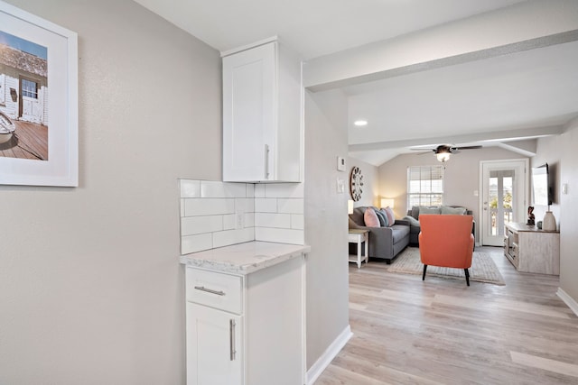 interior space with vaulted ceiling with beams, light stone countertops, ceiling fan, white cabinetry, and light wood-type flooring