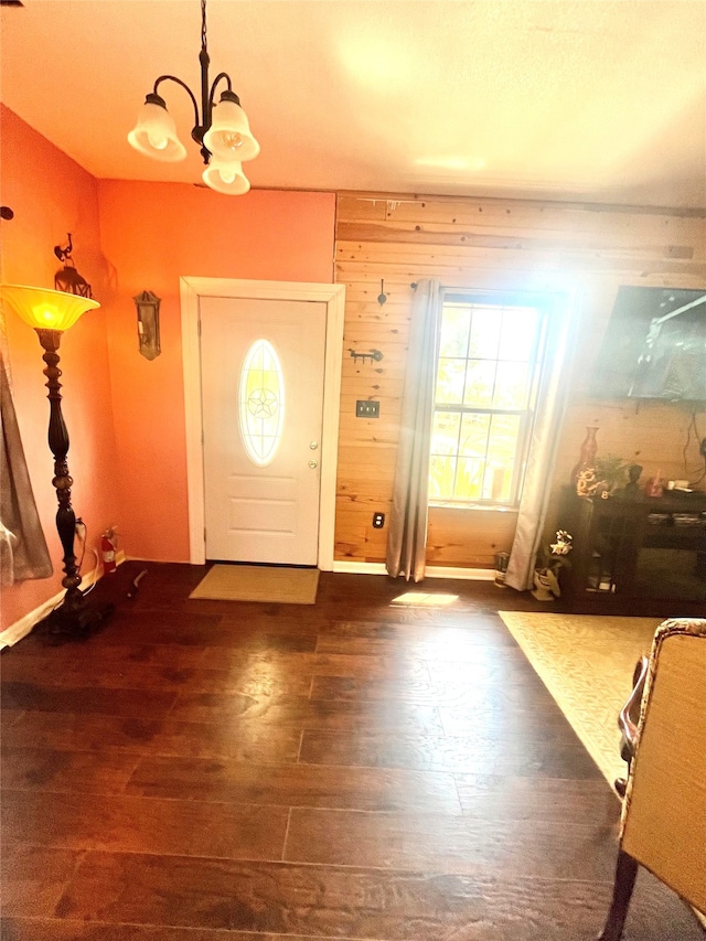 foyer with wooden walls, a chandelier, and dark hardwood / wood-style floors