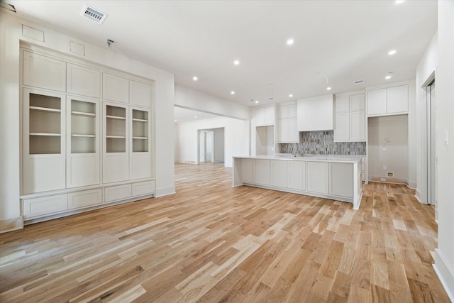 kitchen with white cabinets, an island with sink, light wood-type flooring, and decorative backsplash