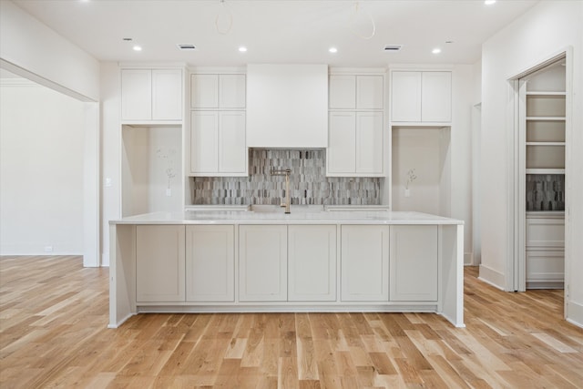 kitchen with white cabinets, backsplash, light hardwood / wood-style floors, and a center island