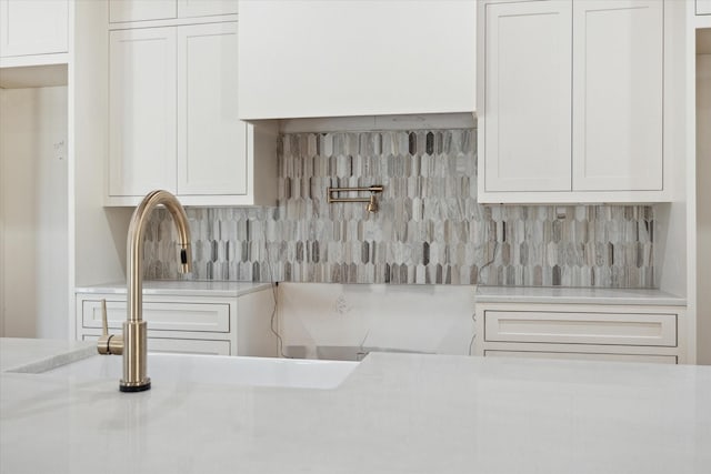 interior details with tasteful backsplash, light countertops, and white cabinetry