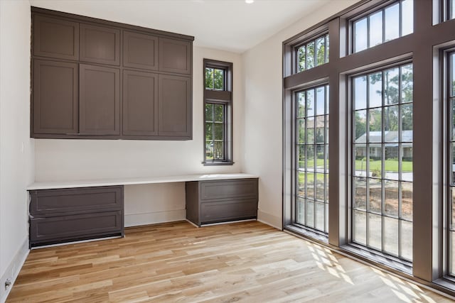 unfurnished office featuring built in desk, light hardwood / wood-style floors, and plenty of natural light